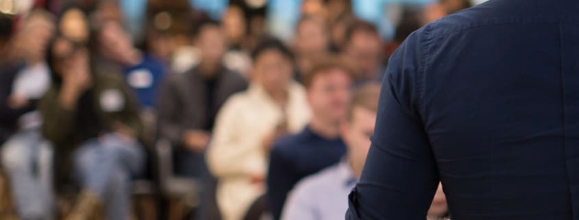 Speaker addressing group. Businessman entrepreneur giving a lecture to a sold-out crowd in a lecture hall. Speaker talking in seminar. Speaker at business conference or presentation stock photo. Male CEO talking during a business presentation in a board room. Copy space. Business coach concept.